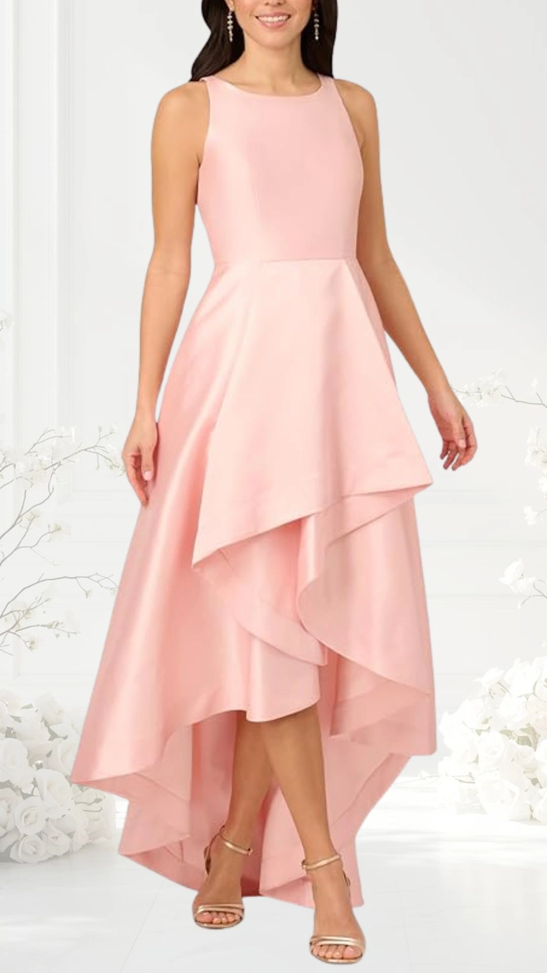 The dress features a blush pink hue with a sleeveless, fitted bodice that flows into an asymmetrical hemline, creating a layered effect. The skirt cascades elegantly, shorter in the front and longer in the back, enhancing its romantic appeal. Paired with strappy gold sandals, this outfit is stylish and sophisticated, perfect for wedding celebrations.