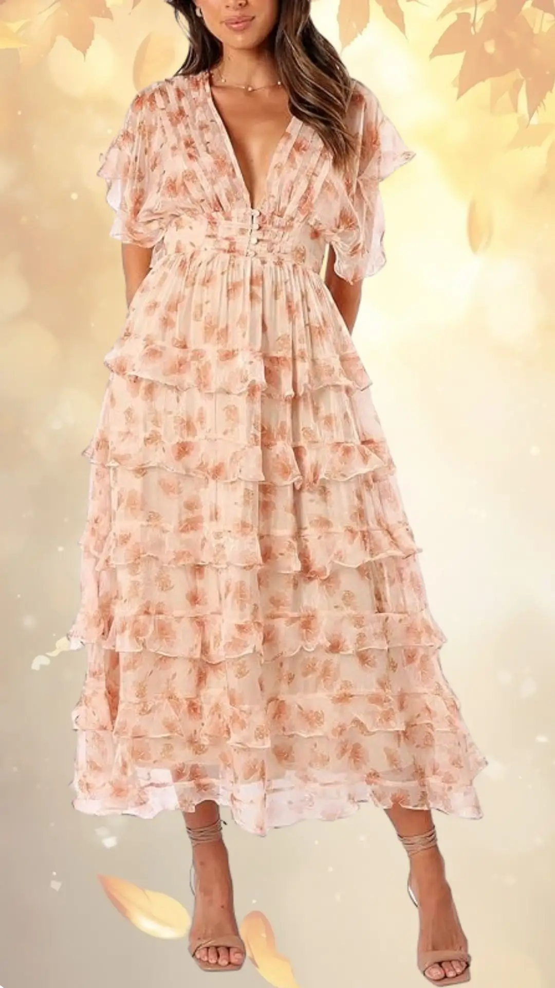 A flowing fall floral wedding guest dress features a soft, blush pink fabric adorned with delicate rose patterns. The dress has a deep V-neckline, short, fluttery sleeves, and multiple ruffled tiers that create a romantic silhouette. It is complemented by strappy, nude high-heeled sandals, adding elegance to the ensemble.