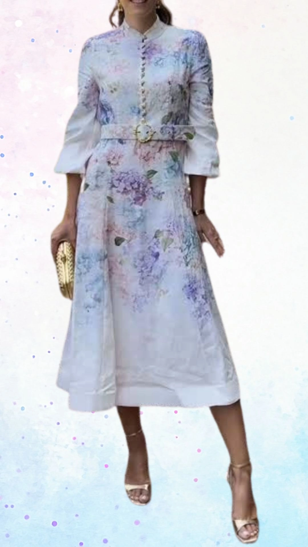 The outfit features a flowing, knee-length dress made from lightweight fabric with a soft floral print in pastel shades of lavender, pink, and blue, evoking a celebratory atmosphere. It has a high neckline, three-quarter sleeves, and a belted waist accentuated by a gold buckle, providing an elegant silhouette. Delicate button detailing runs down the front, while the sleeves and skirt have a slight flare for added movement and comfort.