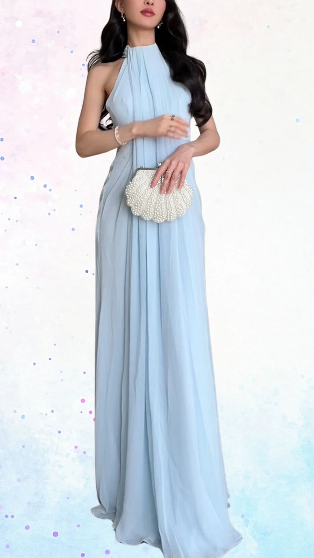The outfit features a flowing, sleeveless gown in soft pastel blue, crafted from lightweight chiffon that drapes elegantly. It showcases a high neckline with delicate pleats and a floor-length silhouette, complemented by a pearl-embellished clutch that adds a touch of sophistication, making it suitable for a baby shower celebration.