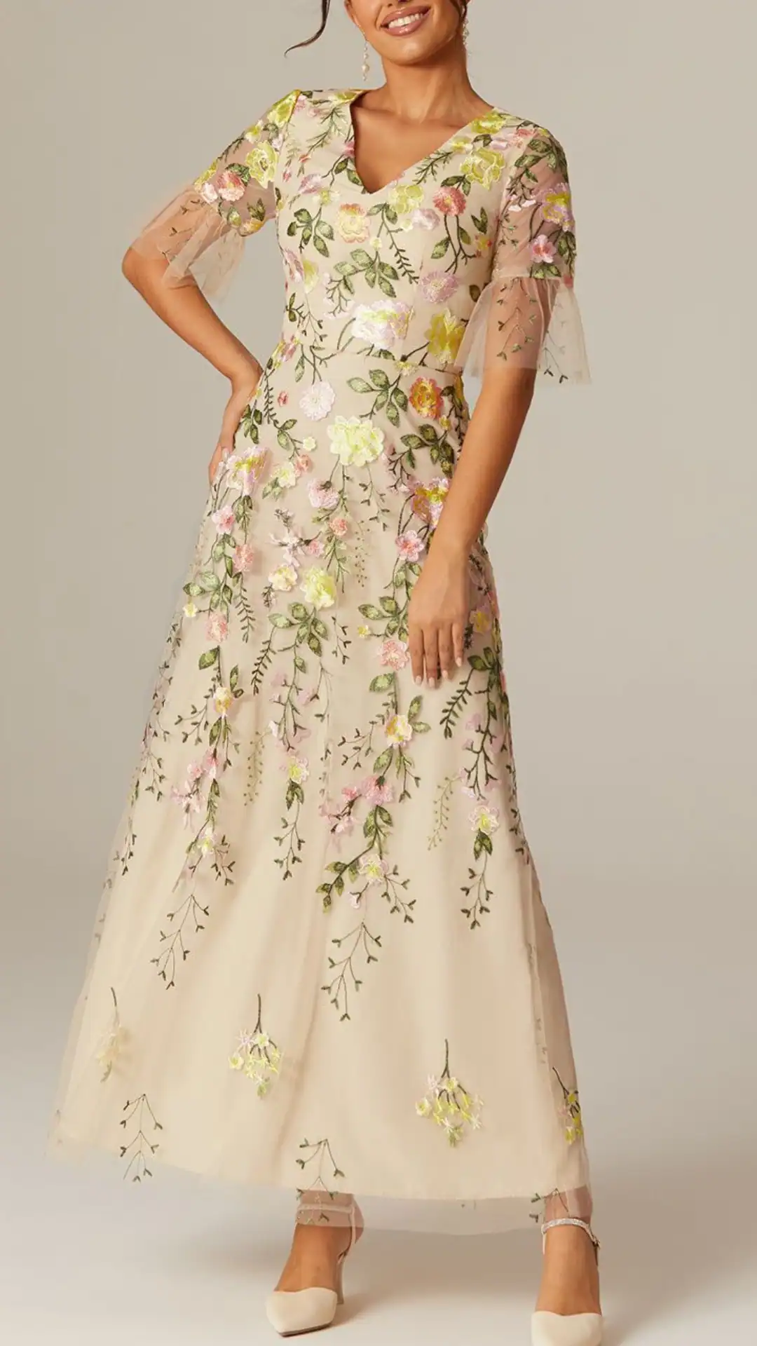 An elegant homecoming dress with a soft beige base featuring vibrant floral embroidery in shades of pink, yellow, and green, perfect for formal events or school dances.