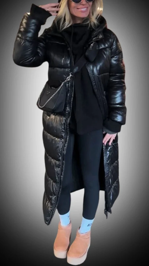 The outfit features a long, shiny black puffer coat with a sleek, modern silhouette and textured horizontal stitching. Underneath, a fitted black hoodie and leggings create a streamlined base, complemented by casual light brown platform boots for added height and comfort. This stylish winter ensemble is both functional and trendy, perfect for staying warm while looking chic.