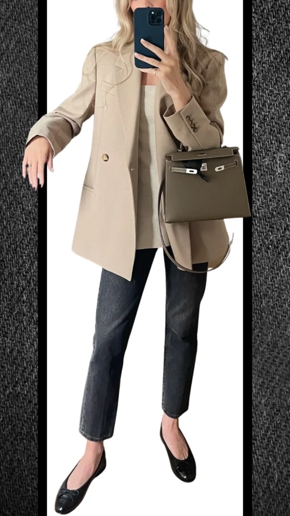 The outfit features tailored black jeans paired with a light beige oversized blazer, providing a chic contrast. Textured black flats add sophistication, while an elegant olive handbag enhances the overall polished look, perfect for cooler months. The combination of materials and shades offers a modern yet timeless winter style.