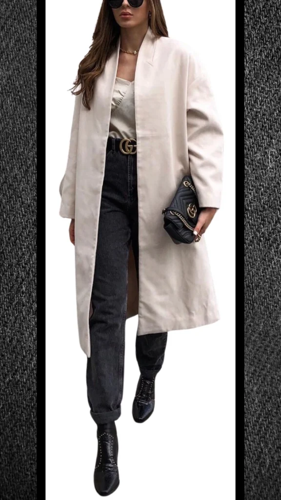 The outfit features a stylish beige trench coat layered over a cream top, paired with high-waisted black jeans that have a soft, textured finish. Complemented by sleek black ankle boots and a chic black handbag with gold accents, this ensemble combines modern elegance and warmth, perfect for winter wear. The contrasts in color and texture enhance its visual appeal while offering comfort for cooler days.