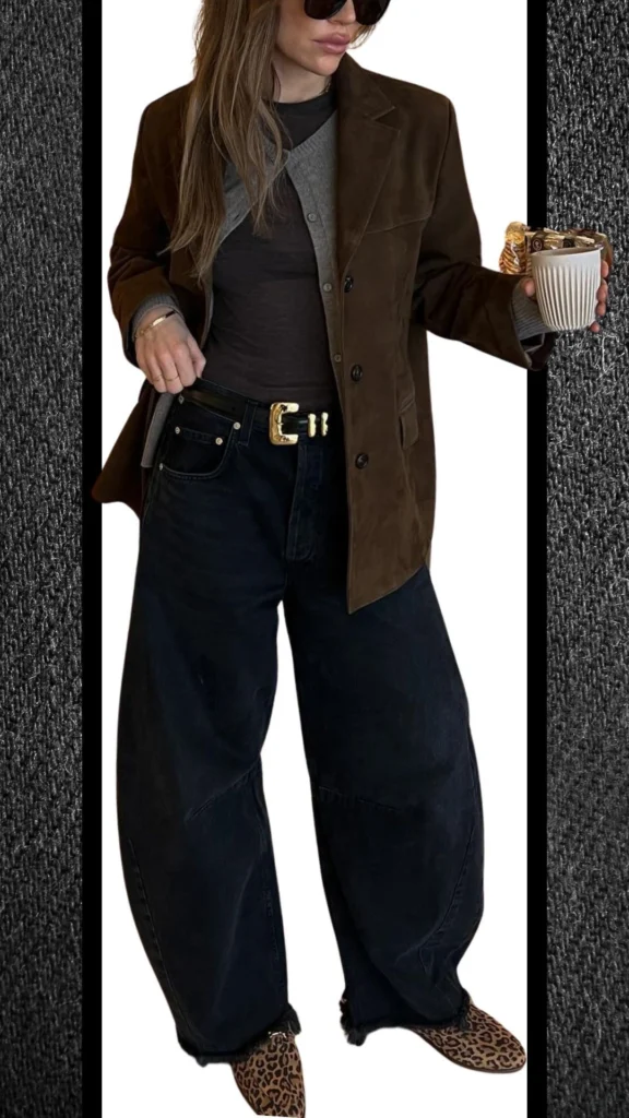 A chic winter outfit featuring high-waisted black jeans with a relaxed fit, paired with a dark brown suede oversized blazer, and a layered light gray cardigan underneath. The look is accentuated by a bold gold belt and stylish leopard print mules, adding texture and a pop of pattern, perfect for cooler months. The combination of neutral and warm shades creates a sophisticated and versatile ensemble.