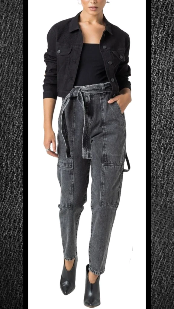 The outfit features a fitted, ribbed black tank top paired with high-waisted, slightly loose black jeans that have a subtle acid wash texture and practical cargo pockets. Layered on top is a cropped black corduroy jacket with a button-up front and long sleeves, while sleek black ankle boots complete the look, offering both style and warmth for cooler weather. The ensemble combines modern cuts with versatile textures, making it a chic choice for winter.