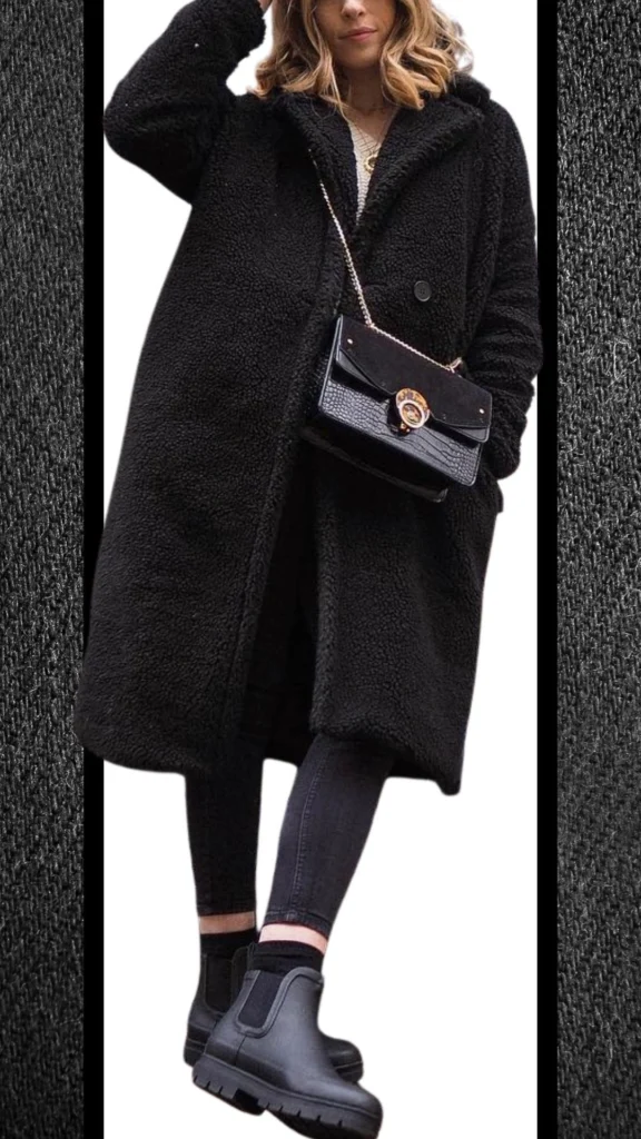The outfit features a cozy, oversized black faux fur coat layered over fitted black jeans, creating a sleek silhouette. Chunky black Chelsea boots add warmth and style, while a structured black handbag with a gold clasp introduces a touch of elegance. This ensemble combines rich textures and deep shades, ideal for winter fashion.