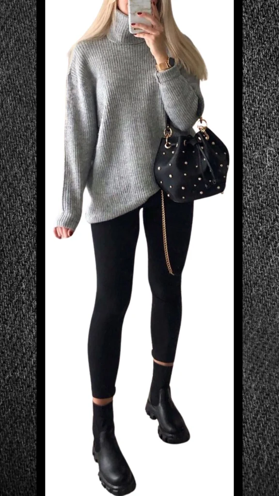 The outfit features a soft, ribbed gray turtleneck sweater paired with form-fitting black leggings, creating a sleek silhouette. Complemented by chunky black ankle boots and a stylish black handbag adorned with gold studs, this ensemble exudes warmth and modern elegance, perfect for winter outings.