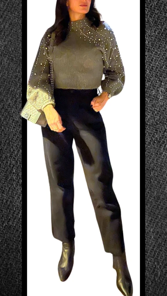 The outfit features high-waisted black jeans that are tailored for a sleek fit, paired with a textured olive green sweater adorned with large pearls for a touch of elegance. Complemented by shiny black ankle boots, the look exudes sophistication, perfect for winter styling. An understated silver handbag adds a modern accessory, enhancing the overall polished appearance.