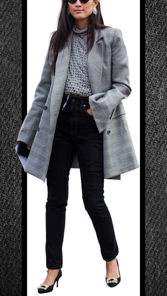 The outfit features high-waisted black jeans with a rugged texture and distressed detailing, paired with a light grey plaid oversized blazer that adds sophistication. Underneath, a fitted, mesh knit top in soft grey provides contrast, while elegant black heels adorned with embellishments elevate the look. Complete with oversized sunglasses, this ensemble is stylish and suitable for cooler months.