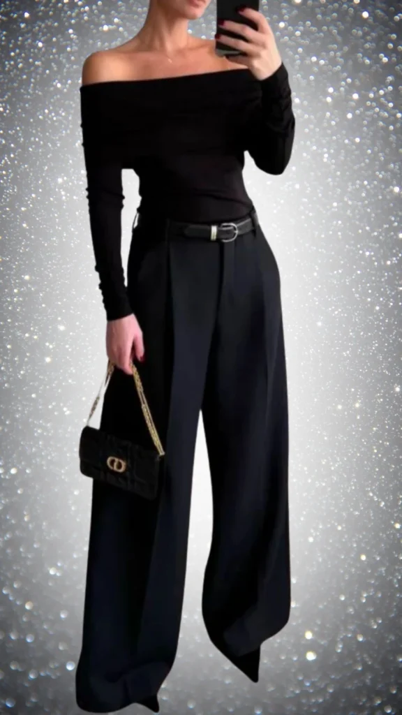 The outfit features a fitted off-shoulder black top crafted from a smooth, lightweight fabric paired with wide-leg black trousers made of a structured material, enhancing elegance. A slim black belt cinches the waist, while a chic black handbag with a gold chain strap adds a touch of sophistication. The overall tonal richness and blend of textures create a stunning all-black ensemble perfect for winter.