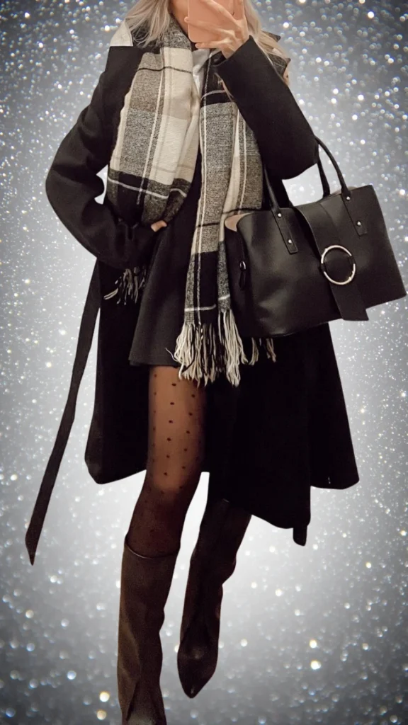 The outfit features a long black coat layered over a black dress, complemented by black polka-dotted tights and knee-high brown boots, creating a sleek silhouette. A textured plaid scarf with black and cream hues adds softness and warmth, while a structured black handbag with a circular accent offers a stylish touch. This elegant all-black ensemble combines rich textures and contrasting patterns, making it ideal for winter.