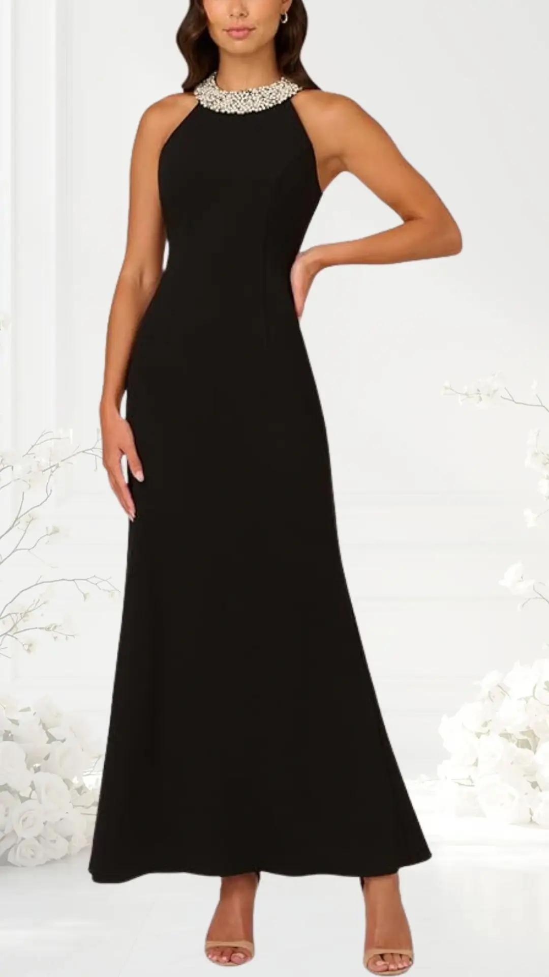 A sleek black evening gown features a fitted silhouette that flares slightly at the hem, showcasing a sophisticated high neckline adorned with a shimmering pearl embellishment. The dress is sleeveless, emphasizing elegant shoulders, and is paired with subtle nude heels.