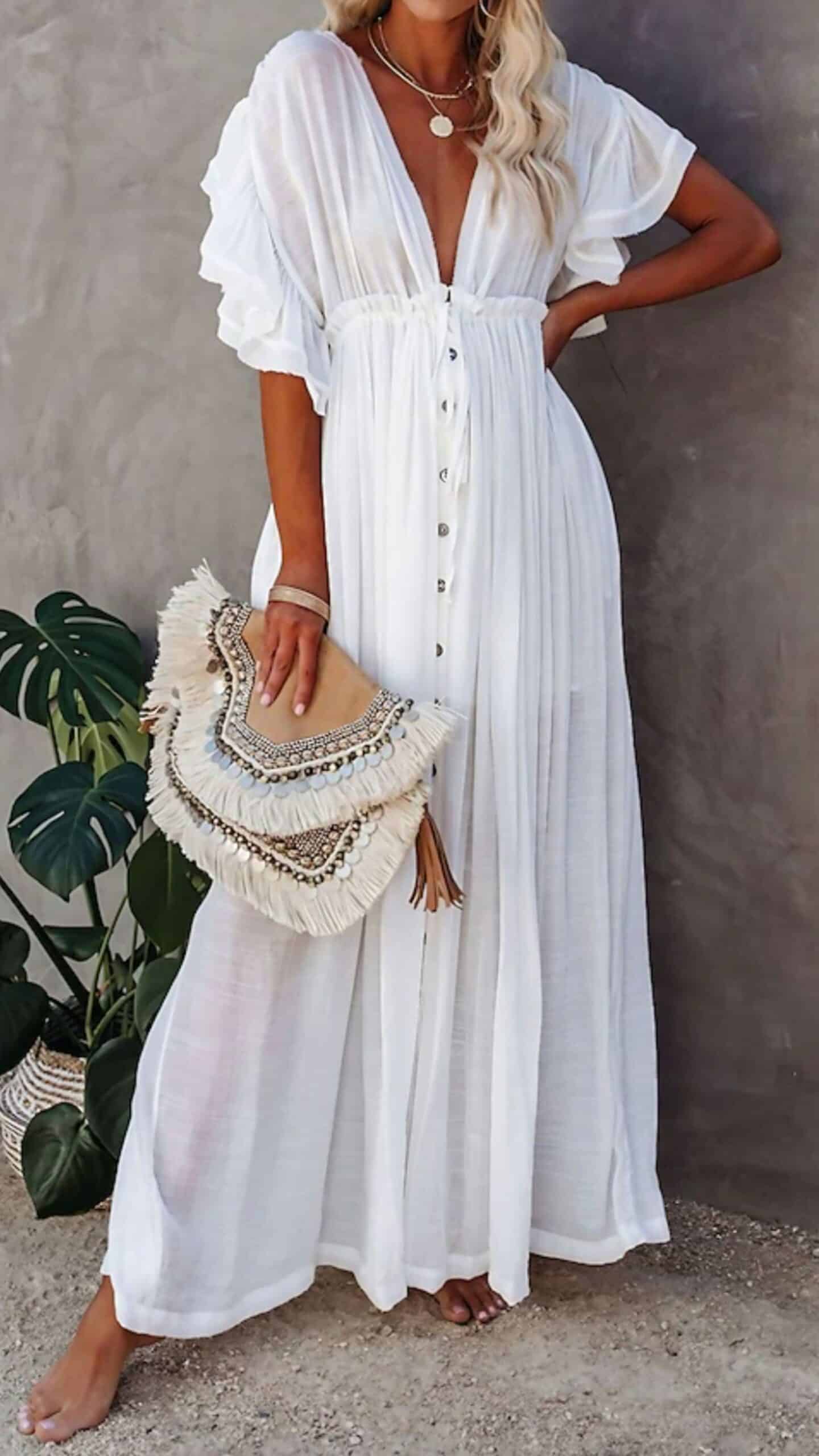 The dress features a flowing maxi silhouette with a deep V-neckline and flutter sleeves, created from a lightweight, textured fabric that gently drapes. This white garment showcases subtle, vertical stripes and falls to the ankle, complemented by button detailing down the front and a relaxed fit that evokes a romantic, bohemian vibe, making it suitable for casual outings or summer gatherings.