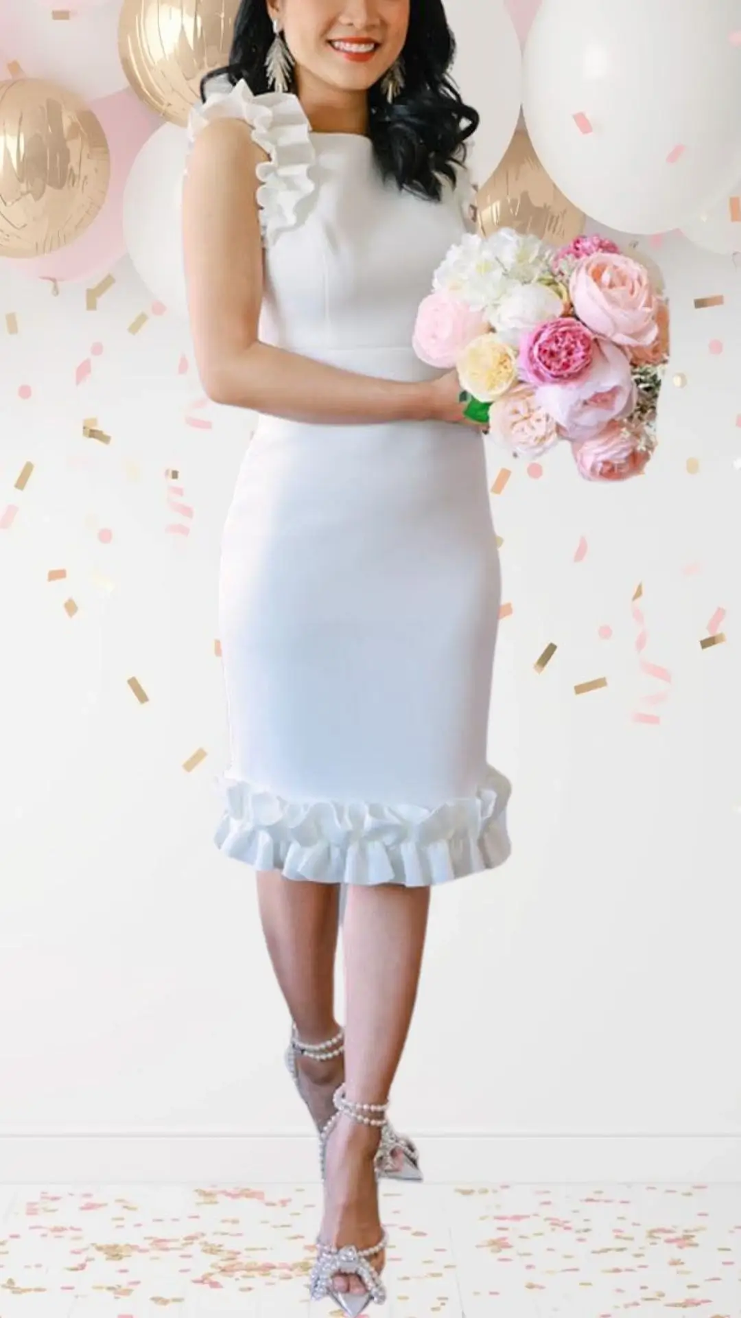 The bridal shower outfit features a chic white dress with a fitted silhouette, crafted from a smooth fabric that enhances its elegance. It includes playful ruffled sleeves and a flouncy ruffled hem at the knee, adding a whimsical touch, while the look is completed with sparkling strappy heels adorned with pearls. The overall design balances sophistication with a festive air, perfect for a celebratory occasion.