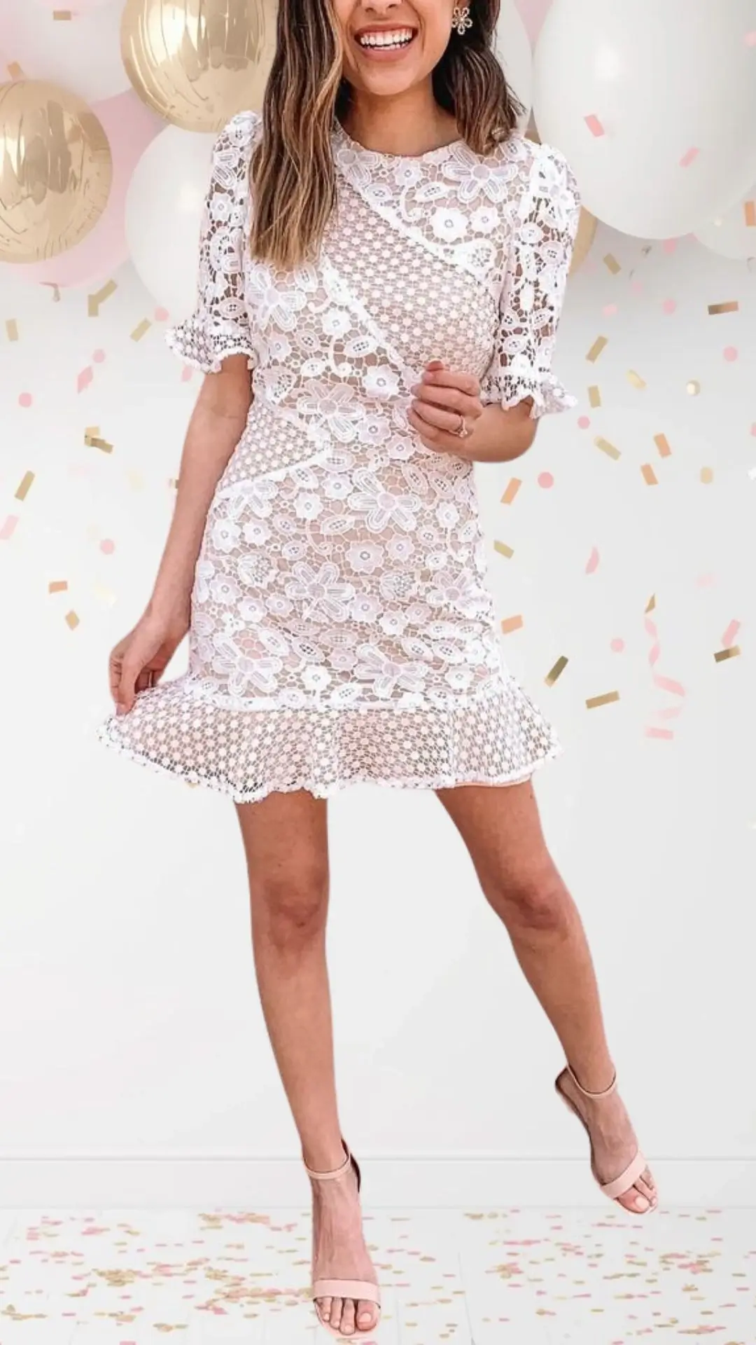 A short, elegant bridal shower dress crafted from delicate white lace, featuring floral patterns and a playful, flared hem. The dress has a modest round neckline, short puff sleeves with scalloped edges, and is layered over a nude lining for added depth, striking a perfect balance between classy and whimsical. Paired with simple nude heels, this outfit embodies celebration and joy.