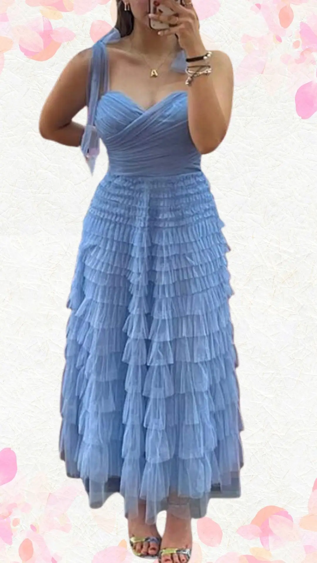 The outfit features a light blue, tiered midi dress crafted from a soft, flowy fabric, adorned with playful ruffles that add whimsy. It has a sweetheart neckline and delicate, adjustable spaghetti straps, combining a sense of elegance with a joyful, celebratory vibe. The layered structure creates texture while maintaining an appropriate balance between formal and casual.