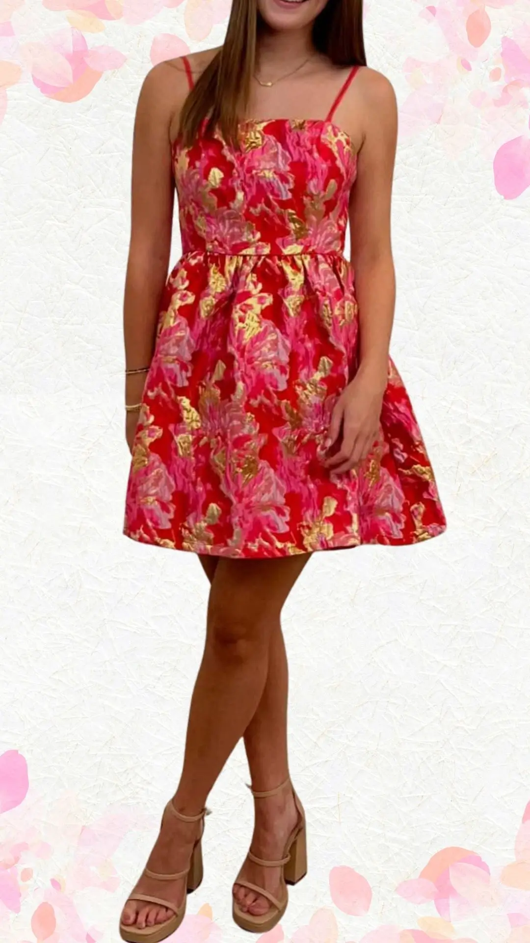 The outfit features a vibrant red dress adorned with bold pink and gold floral patterns, crafted from a lightweight, textured fabric. It showcases a fitted bodice with delicate spaghetti straps and a playful flared skirt that falls just above the knees, enhancing its celebratory feel. The dress is elevated by the combination of intricate pleats and a subtle shimmer, complemented by nude block-heeled sandals for a chic yet approachable look.