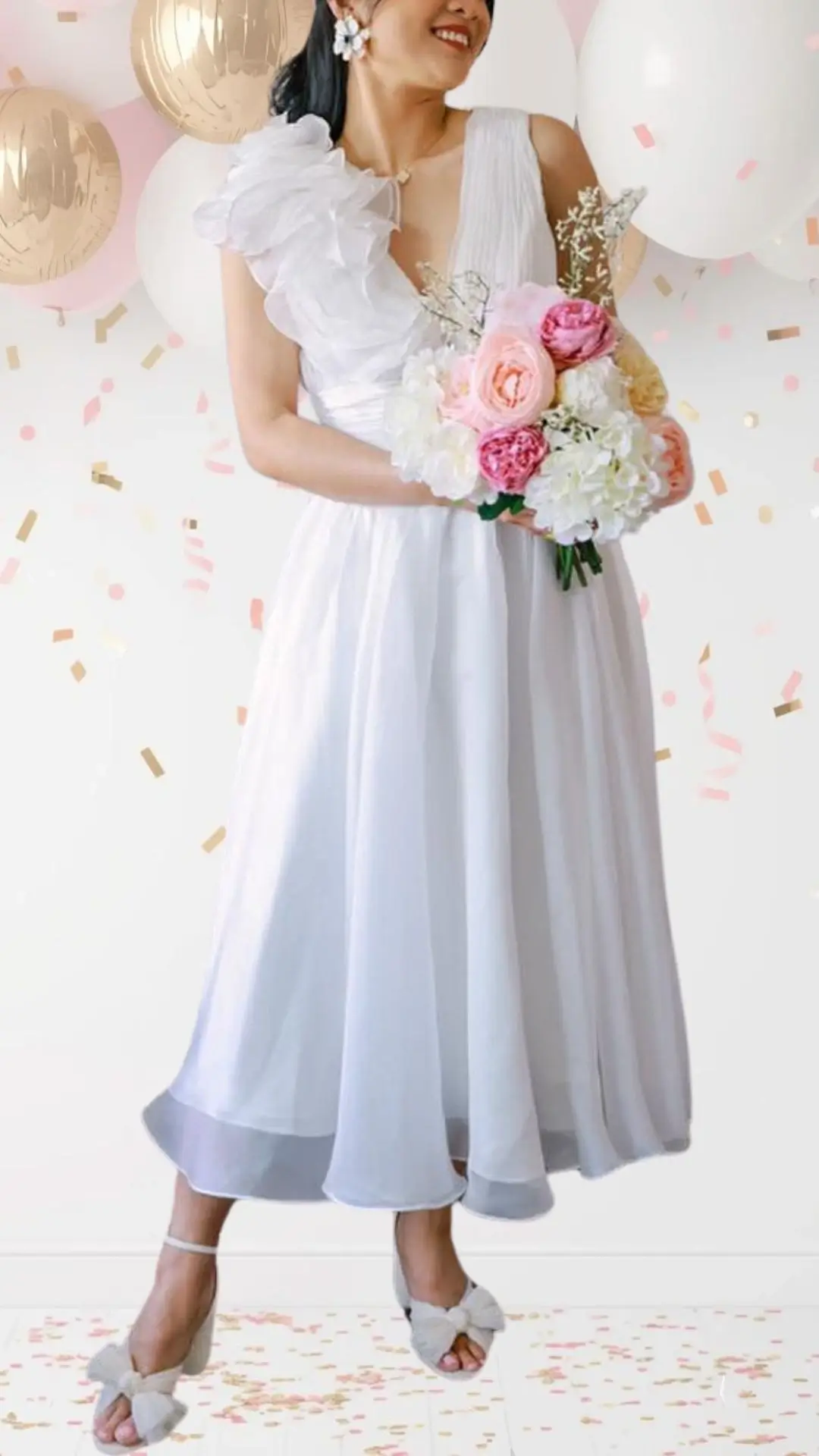 The outfit features a flowing white dress with a fitted bodice and an elegant, asymmetrical ruffled shoulder, complemented by a soft pleated skirt that falls below the knee. The fabric has a light, airy texture, creating a whimsical feel, while the deep V-neckline adds sophistication. Paired with delicate sandals adorned with bows, this ensemble strikes a balance between classy and playful, perfect for a bridal shower celebration.