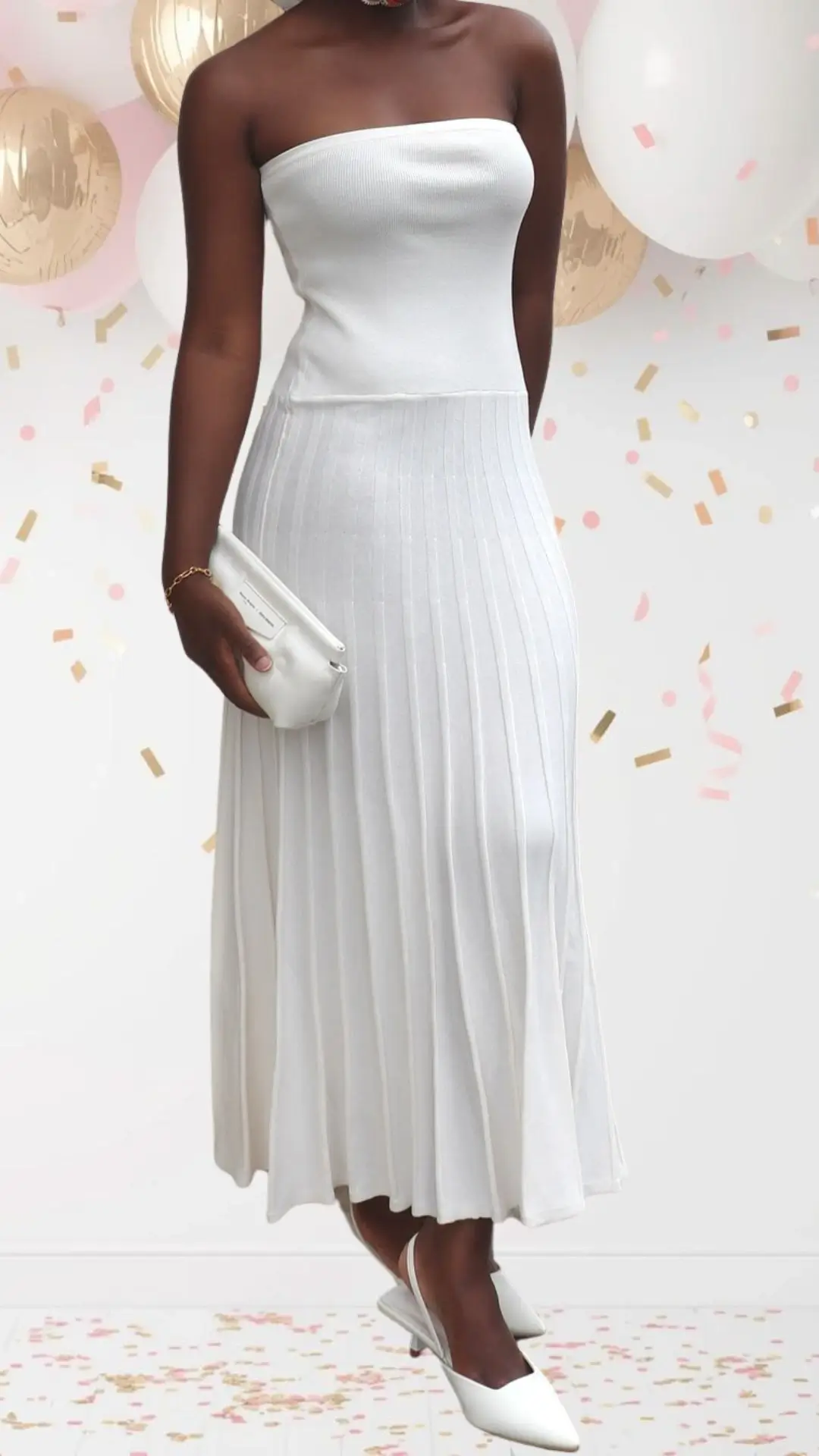 The bridal shower outfit features a fitted, strapless white dress made from ribbed fabric, transitioning into a pleated A-line skirt that flows gracefully. The sleek neckline and mid-calf length create an elegant silhouette, while matching white slingback heels and a chic clutch add a polished yet playful touch to the celebratory look.