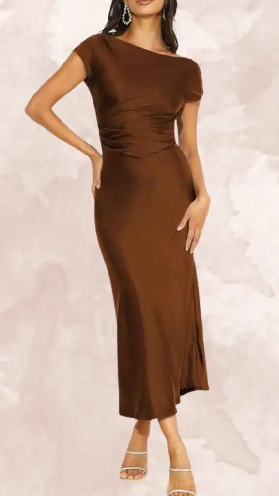 This brown bridesmaid dress features a flattering off-the-shoulder neckline and short cap sleeves, accentuating the waist with stylish ruching. The dress has a sleek, midi length and a high slit on one side, creating a sophisticated silhouette. Crafted from a smooth, solid chocolate brown fabric, it presents an elegant and timeless look suitable for any wedding occasion.