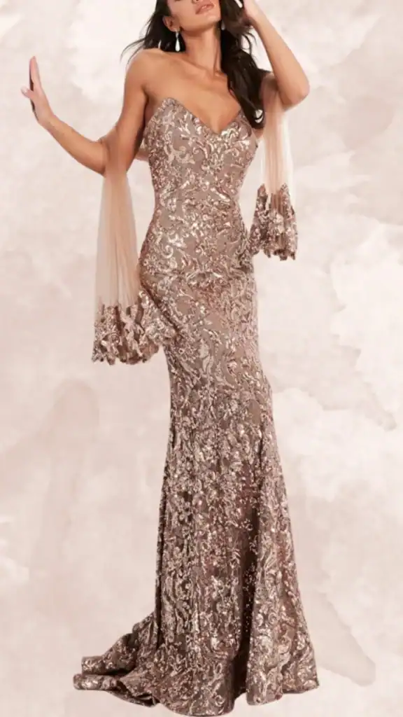This brown bridesmaid dress features a fitted silhouette with a sweetheart neckline and no sleeves, gracefully flowing into a mermaid skirt that flares out at the hem. The gown is adorned with intricate metallic embroidery in shades of bronze and gold, creating a luxurious effect, while sheer fabric drapes elegantly from the shoulders. The combination of textures and shimmering details adds sophistication to the overall look, making it ideal for formal occasions.