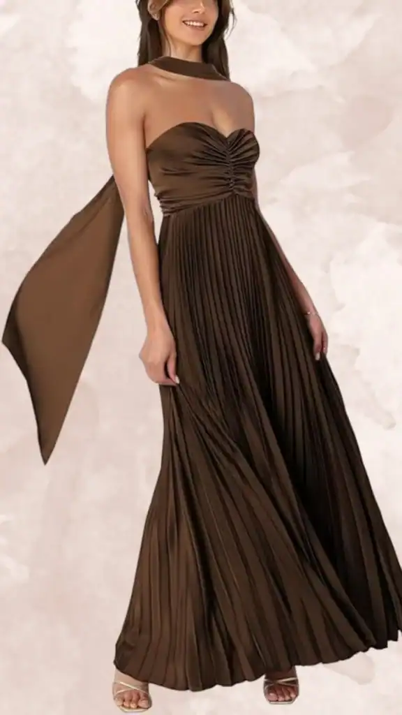 The dress features a structured, strapless design with a sweetheart neckline and a pleated bodice, draping gracefully down into a floor-length, flowing skirt. A unique detail is the wide, matching sash that cascades from the neckline, adding elegance. The rich, deep chocolate brown color creates a timeless look, perfect for bridal parties.