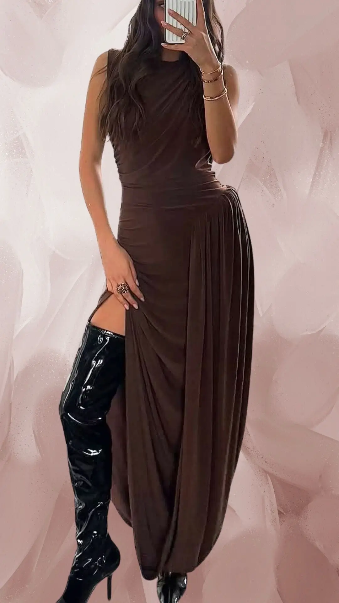 The outfit features a long, draped brown dress made from a soft, stretchy fabric, showcasing a sleek, fitted silhouette and an elegant high neckline. It is complemented by thigh-high glossy black boots that add a bold contrast, while the dress's subtle pleats create movement and visual interest. The overall look exudes sophistication with a modern edge.