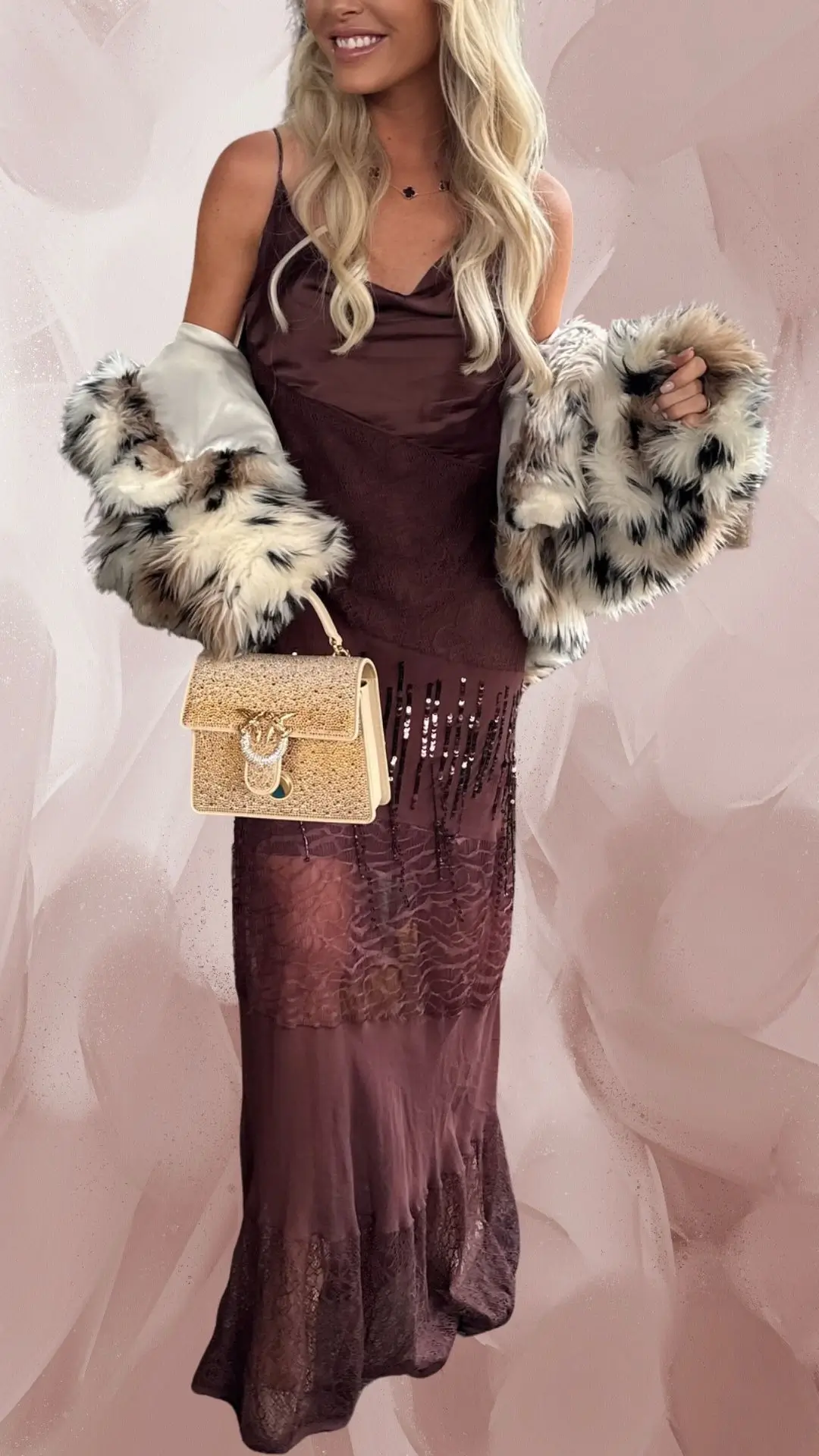 The outfit features a long, flowing brown dress with a combination of satin and lace textures, showcasing a subtle sheen and intricate lace detailing at the hem. It has thin spaghetti straps and a soft cowl neckline, paired with a glamorous faux fur shawl for warmth and elegance. Complemented by a stylish gold-toned handbag, the dress exudes sophistication and can be attributed to formal occasions.