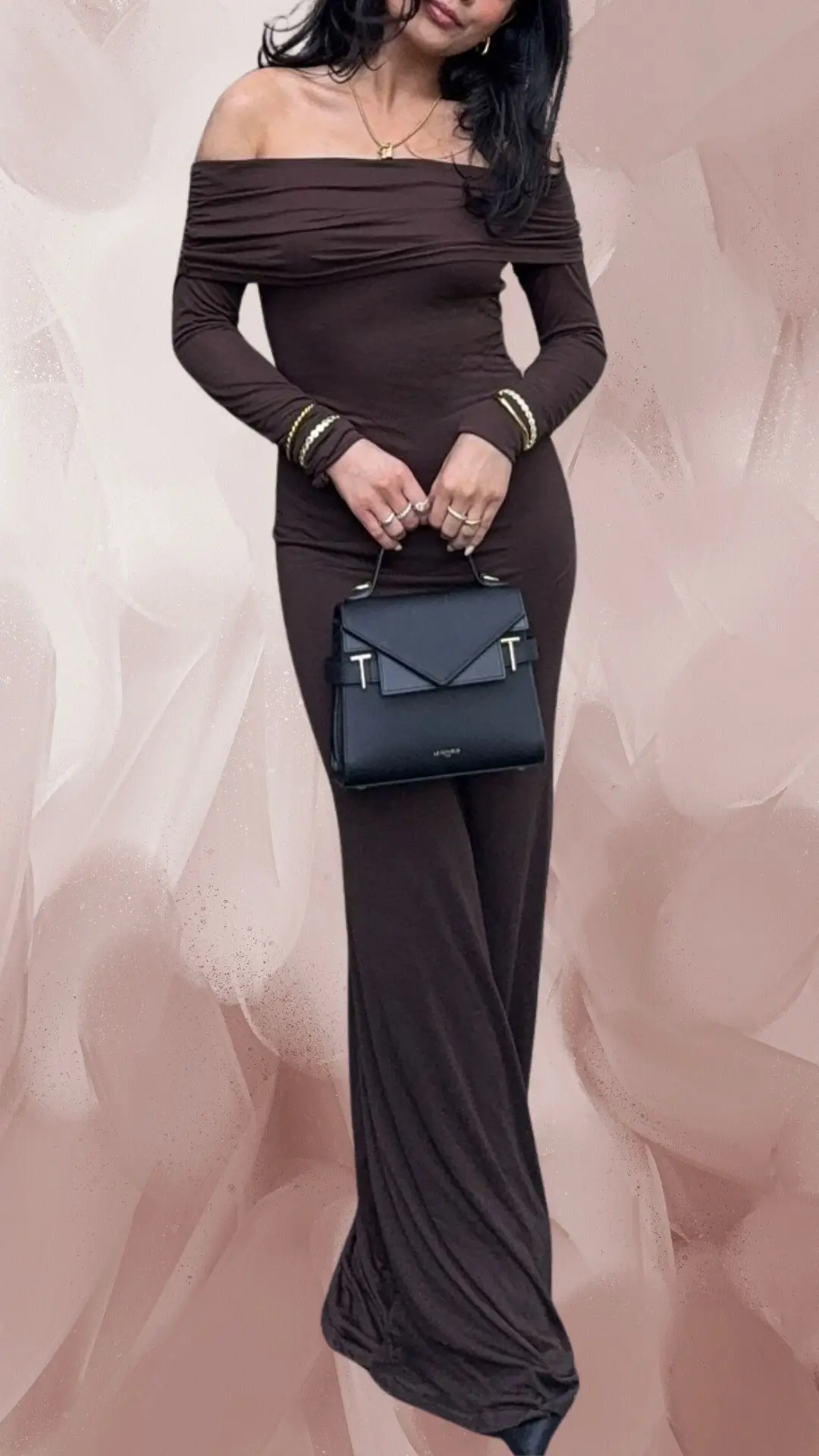 The outfit features a long brown off-the-shoulder dress made from a soft, draping fabric that accentuates the figure. It has long fitted sleeves and a sleek silhouette that falls gracefully to the floor, complemented by gold-accented bracelets and a chic black handbag. The ensemble exudes elegance, making it suitable for formal occasions.
