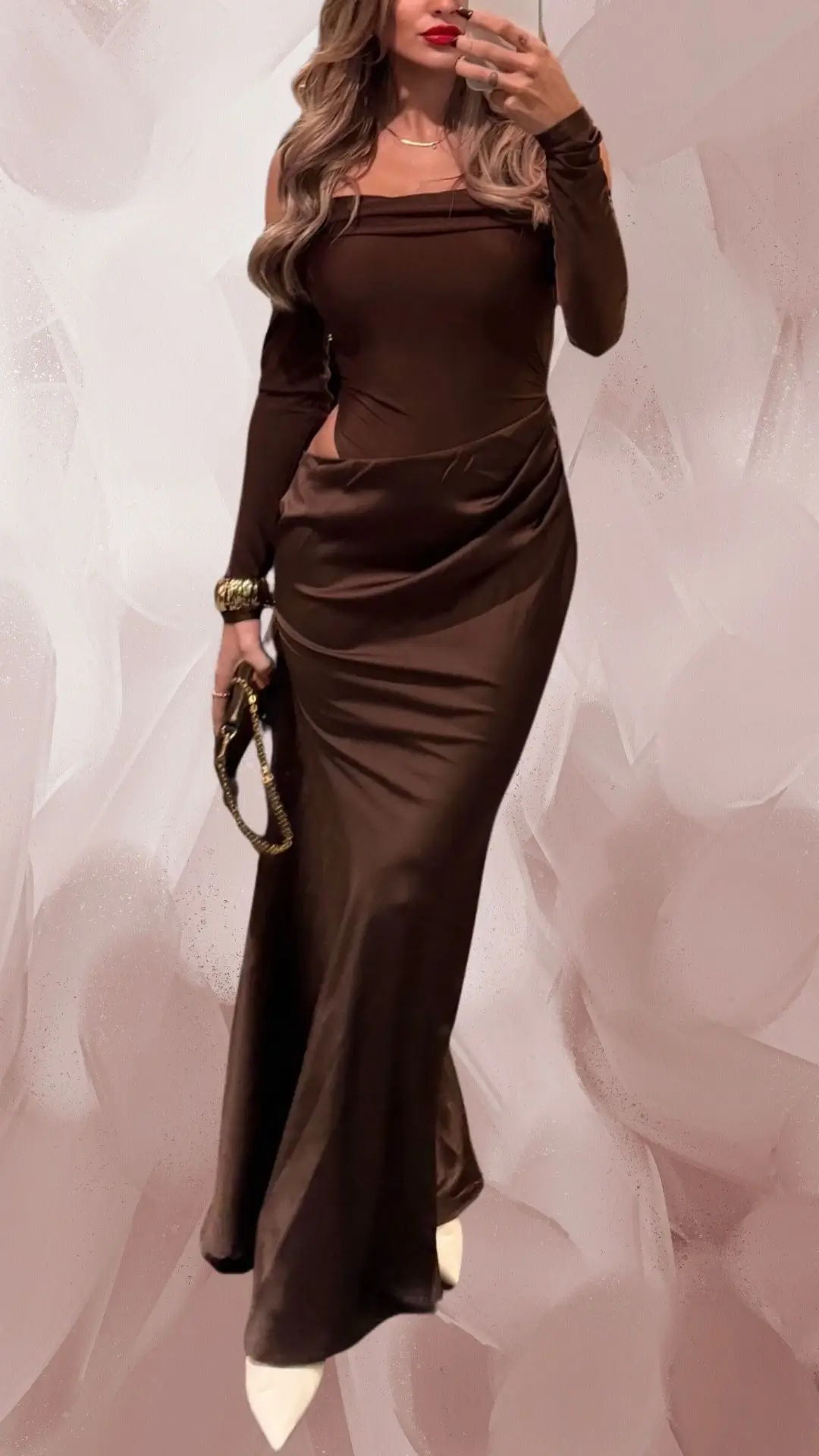 The outfit features a sleek, long brown dress made from a smooth, flowing fabric that elegantly drapes to the floor. It has a square neckline, long fitted sleeves, and stylish cut-outs at the waist, paired with pointed white heels that add a modern contrast. Accessorized with a gold bracelet and a chic clutch, this ensemble exudes sophistication and contemporary flair.