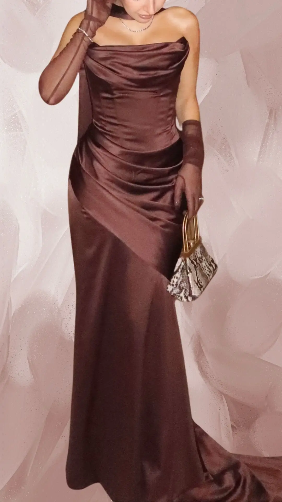 The outfit features a sleek, strapless brown satin gown that hugs the body and flows elegantly to the floor. It includes sheer, fitted brown gloves and is complemented by a stylish, small handbag with a snake-print design. The dress showcases a smooth texture with subtle draping that enhances its sophisticated appeal.
