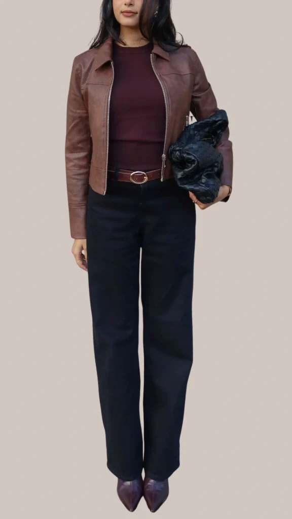 A sleek brown leather jacket with a slightly textured finish is paired with a fitted burgundy top, emphasizing a chic silhouette. The outfit is completed with tailored black wide-leg trousers and pointed-toe burgundy heels, while a stylish black woven clutch adds a touch of elegance. This combination showcases a harmonious blend of luxurious tones and contemporary textures.