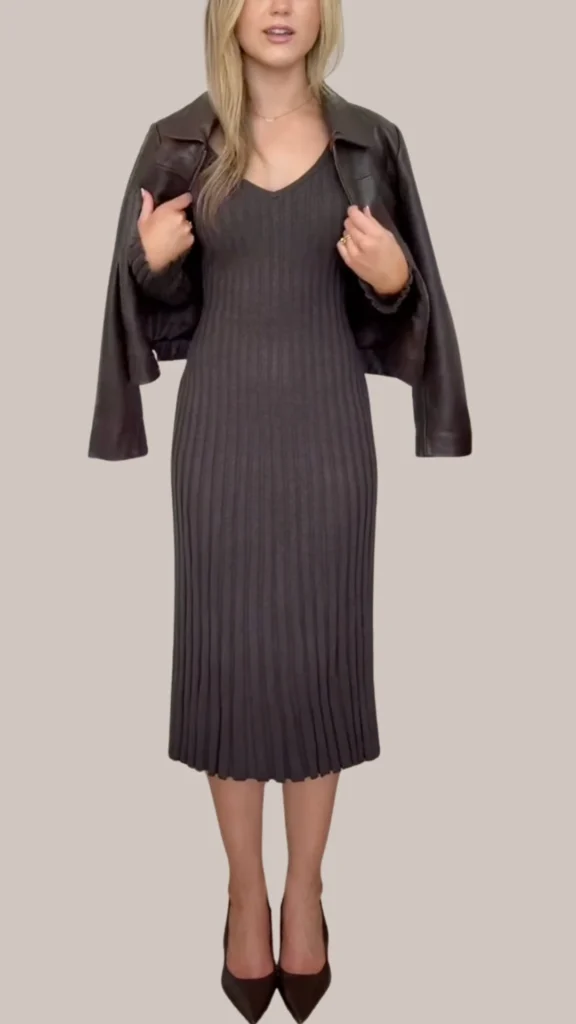 A chic brown leather jacket is draped over a figure-hugging, dark ribbed dress that features subtle vertical pleats, enhancing its elegant texture. The outfit is completed with sleek, dark brown pointed-toe heels, adding sophistication and class to the ensemble. The rich brown tones of the leather and the dress create a refined monochromatic look perfect for a stylish outing.