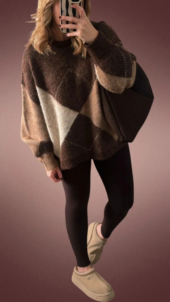The outfit features brown leggings made from a soft, stretchy fabric, paired with an oversized, cozy sweater in rich shades of brown and beige, showcasing a stylish geometric pattern. Complementing the look are beige slip-on shoes with a fleece lining for added warmth and comfort, along with a textured dark brown handbag. This ensemble is ideal for winter, offering both warmth and a relaxed fit.