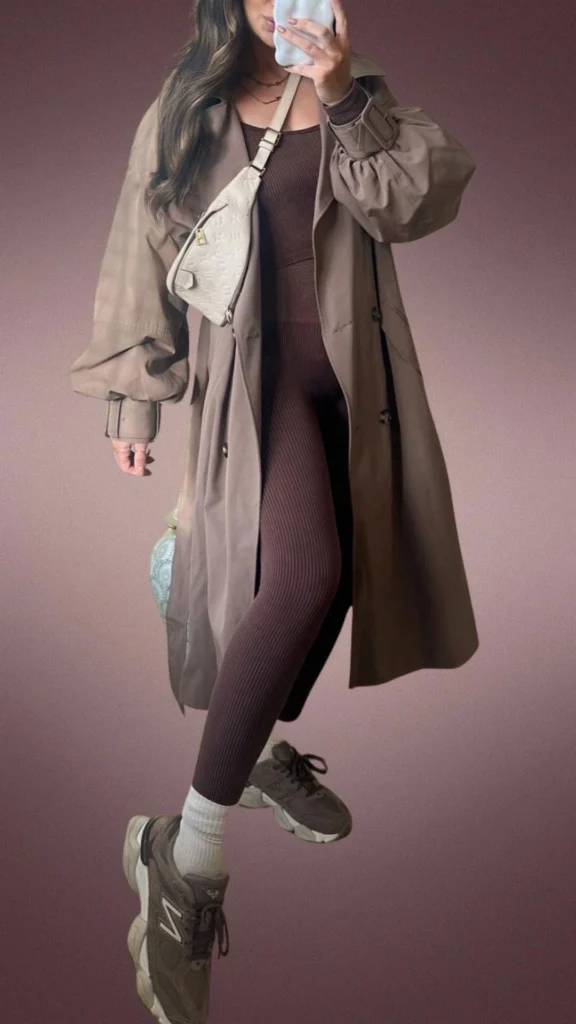 The outfit features snug, ribbed brown leggings paired with a long, relaxed-fit brown coat that has voluminous sleeves, creating a cozy look ideal for cooler months. Complementing the ensemble are chunky brown sneakers and a small light beige crossbody bag, adding both style and comfort. This combination emphasizes a warm, earthy palette that is perfect for winter layering.
