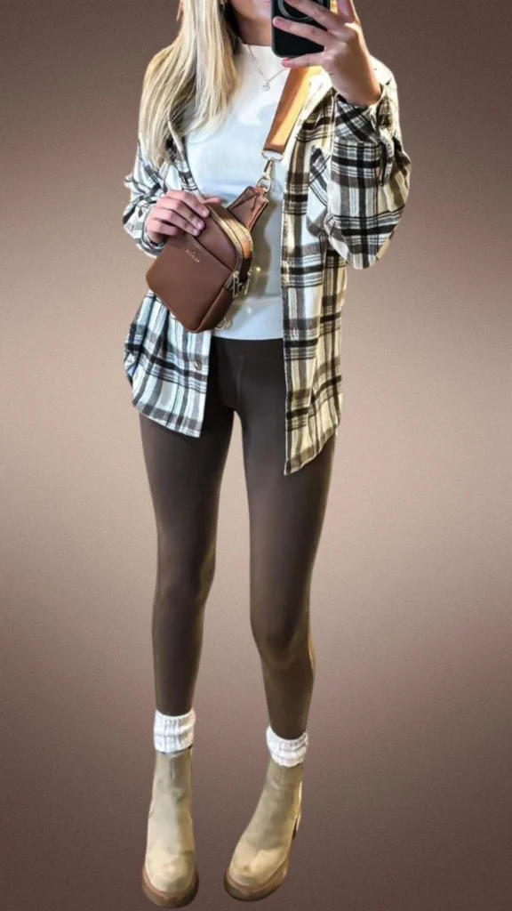 A cozy winter outfit featuring smooth, snug brown leggings paired with a soft, fitted white top and an oversized plaid flannel shirt in cream and brown tones. Complemented by taupe ankle boots and a small brown crossbody bag, this ensemble balances comfort and style, ideal for cooler months. The look is cozy and functional, providing both warmth and versatility.
