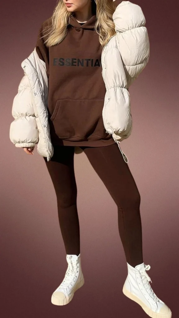 The outfit features soft, brown leggings paired with a matching oversized brown hoodie, complemented by a cozy, puffy off-white winter jacket for added warmth. The fabric is smooth and stretchy, providing comfort and ease of movement, while the white high-top shoes add a stylish contrast. This ensemble is perfect for winter, combining comfort, style, and a snug fit.