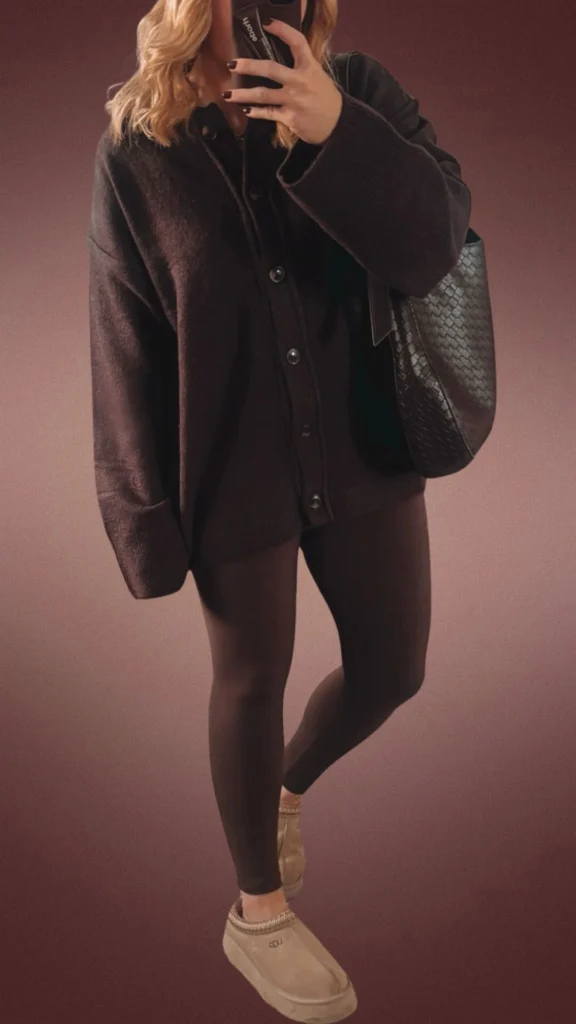 A cozy winter outfit featuring dark brown leggings made from a soft, stretchy fabric that hugs the legs comfortably. The ensemble is paired with an oversized, button-up sweater in a matching rich brown hue, offering warmth and a relaxed fit, complemented by plush beige slippers for added comfort. A textured black tote bag adds a stylish touch while maintaining functionality.
