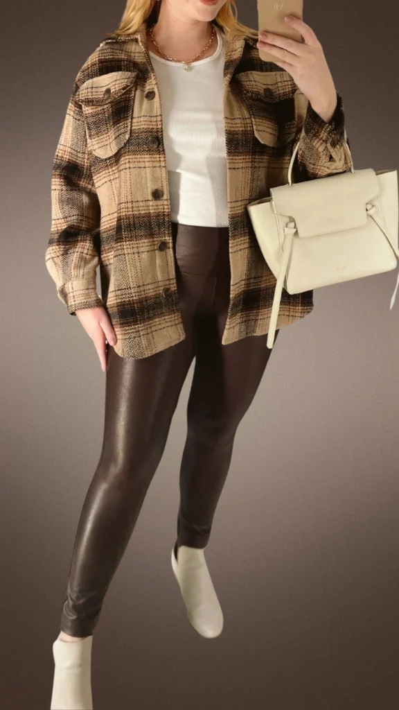 The outfit features sleek, dark brown leggings made from a stretchy, cozy material paired with a soft, plaid shacket in shades of beige and black, adding warmth and texture. Underneath, a fitted white ribbed top provides a contrasting brightness, while stylish beige slip-on boots and a chic cream handbag complete the look, perfect for winter comfort. The combination of textures and earthy tones ensures a stylish yet cozy ensemble.