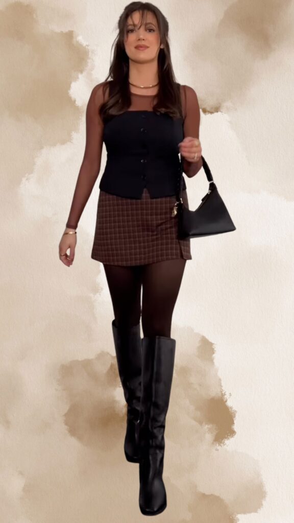 The outfit features a fitted, brown plaid mini skirt paired with a sheer, long-sleeved brown top layered under a sleek black vest. Knee-high black heeled boots complement the look, which is accessorized with a simple gold necklace and a small black handbag, creating a chic and sophisticated ensemble.