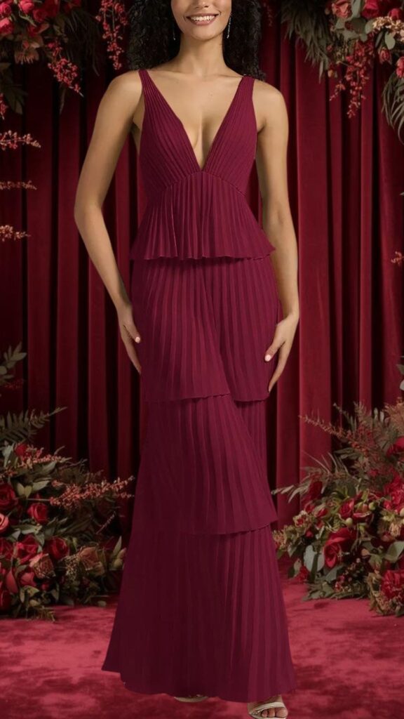 This burgundy bridesmaid dress features a deep V-neckline and no sleeves, showcasing an elegant silhouette. The dress is made from flowing, pleated fabric with layered tiers that create a graceful movement, perfect for a wedding setting. The rich color adds sophistication, making it an ideal choice for bridesmaids.