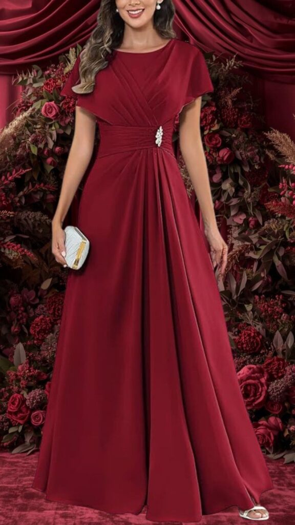 This elegant burgundy bridesmaid dress features a modest round neckline and flutter sleeves that enhance the soft, flowing silhouette. The fabric is smooth and drapes beautifully, with intricate pleats and a tasteful embellishment at the waist, while the floor-length skirt offers a classic look perfect for a wedding.