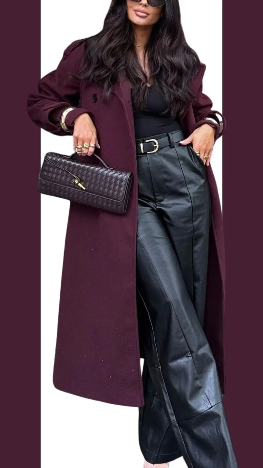 A burgundy trench coat with a relaxed fit features a slightly oversized silhouette and elegant lapels, complemented by a fitted black top underneath. The outfit includes high-waisted black leather pants that offer a chic texture contrast, while stylish ankle boots complete the look. Accented with gold jewelry and a textured dark handbag, this ensemble exudes sophistication and modern flair.