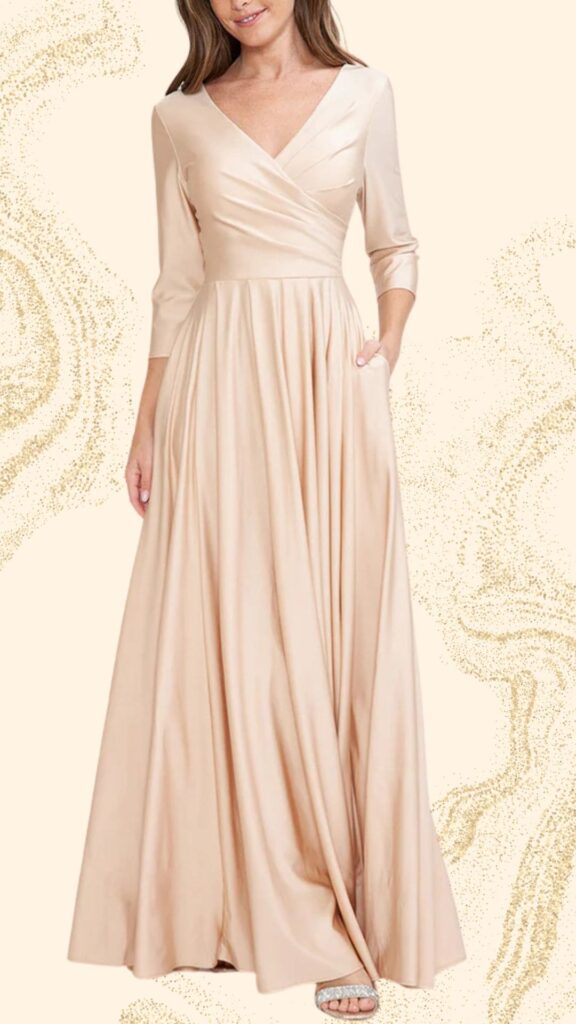 The champagne mother of the bride dress features a floor-length, flowing silhouette crafted from a smooth, satin-like fabric. It is designed with a deep V-neckline and three-quarter sleeves, accentuated by a flattering wrap detail at the bodice and soft pleats that create elegant draping. This gown also includes discreet side pockets for added functionality without compromising its sophisticated look.