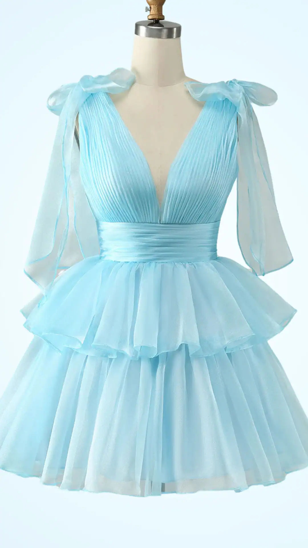 This chic homecoming dress features a delicate light blue hue with soft pleating and flowing layers of sheer tulle for an ethereal, fairytale vibe. Designed with a plunging neckline and fluttery sleeves, it offers a playful fit-and-flare silhouette perfect for teenage girls attending a formal event or school dance.