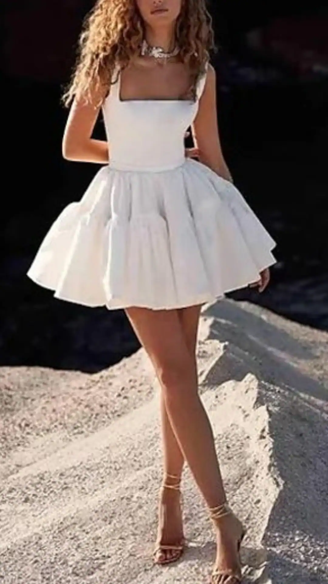 This chic white homecoming dress features a structured square neckline and a voluminous, tiered skirt that creates an airy, playful silhouette. Made from a lightweight fabric, it exudes a fresh, youthful vibe, perfect for a teen attending a party or school dance.