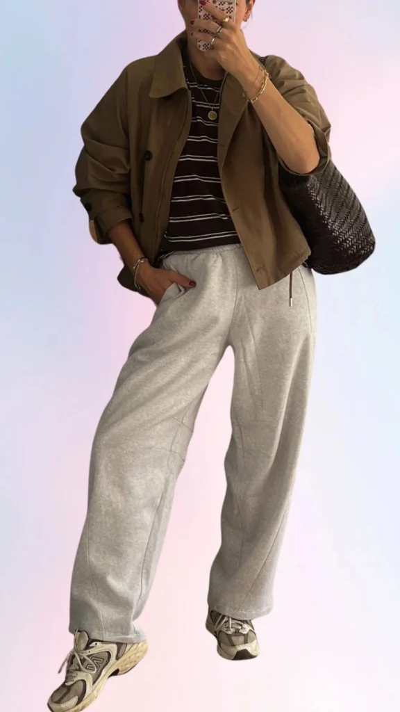 The outfit features a relaxed brown oversized jacket paired with a dark striped t-shirt, creating a cozy look. The comfy gray sweatpants add an effortlessly laid-back vibe, while colorful sneakers complete the relaxed ensemble. This combination highlights soft textures and neutral tones, perfect for easy, stylish days at home or out.