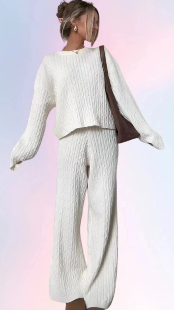 This cozy outfit features a soft, cream-colored oversized cable-knit sweater paired with relaxed-fitting matching pants, both made of a warm and textured fabric that exudes comfort. The outfit's loose silhouette and subtle ribbing create a laid-back aesthetic, while the addition of a simple brown handbag adds a touch of style to the casual look. Perfect for a lazy day, this ensemble balances comfort and effortless chic.