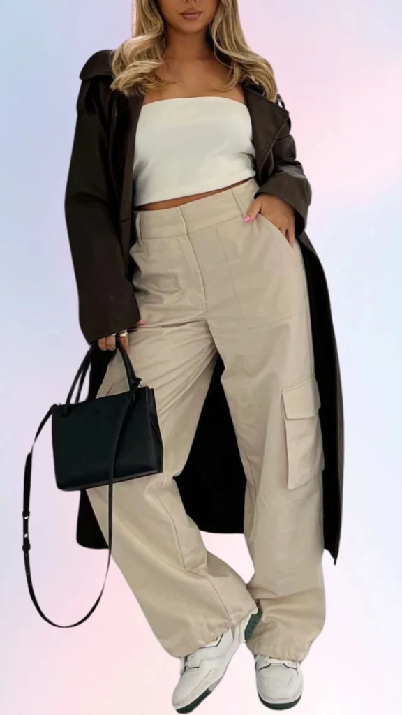 The outfit features a cozy cropped white strapless top paired with relaxed, high-waisted beige cargo pants, accentuating a laid-back vibe. Layered over is a loose-fitting dark brown coat, adding a touch of sophistication while maintaining comfort. The look is completed with casual white sneakers that provide an effortlessly stylish finish.